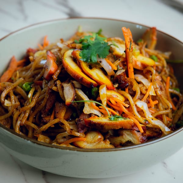 Close-up of Indian noodles with chicken, carrots, onions, and cilantro in a light bowl.