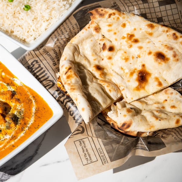 Indian butter chicken, naan bread, and rice with peas on a marble table.